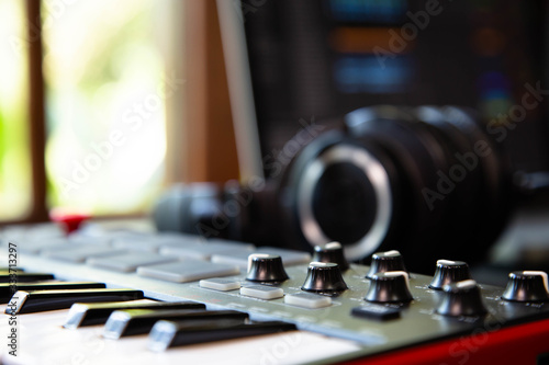 Midi keybard in a music producer home studio, desk with headphones and a notebook. Window with nature in the background.