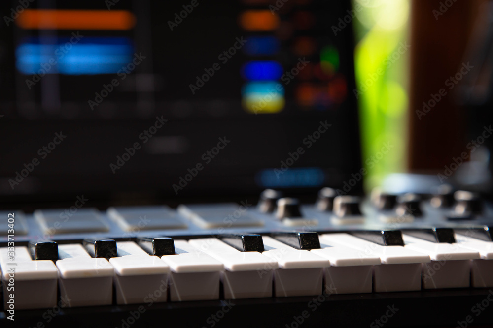 Close up of a Midi keyboard in a music producer home studio. Laptop screen in the background.