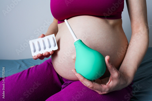 A pregnant girl holds an enema and rectal candles in front of her. suppository. photo