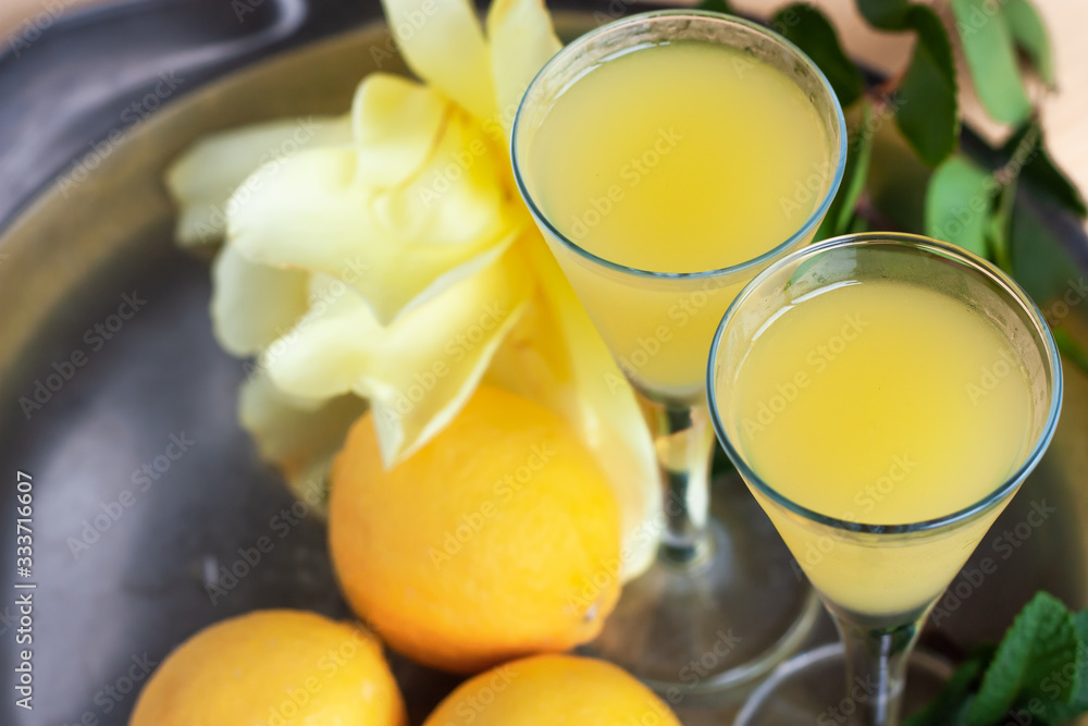 Limoncello in elegant liquor glasses with lemons, mint and yellow rose on steel plate. Sicilian lemon liquor aromatic and refreshing. Top view Limoncello in elegant liquor glasses with lemons, mint and yellow rose on steel plate. Sicilian lemon liquor aromatic and refreshing. Top view