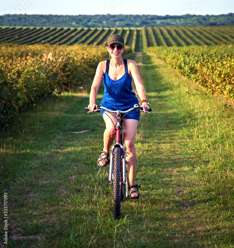 Fototapeta Naklejka Na Ścianę i Meble -  Carefree smiling girl cycling alone in a field among currant bushes in the garden. the best solution to escape from a coronavirus