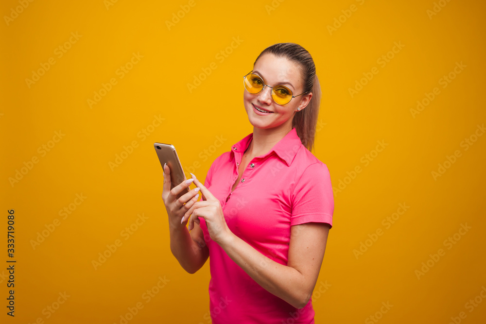 Bright and positive young woman with smartphone on yellow background. The girl uses a smartphone Bright and positive young woman with smartphone on yellow background. The girl uses a smartphone