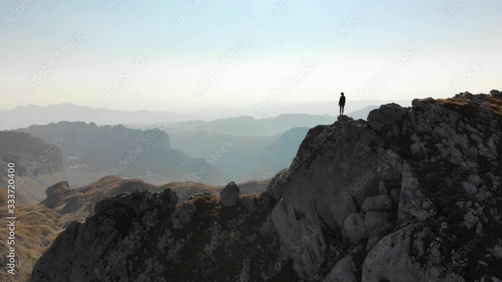 Girl standing on a mountain ridge. Beautiful aerial view of the peaked tops of Durmitor in Montenegro Girl standing on a mountain ridge. Beautiful aerial view of the peaked tops of Durmitor in Montenegro