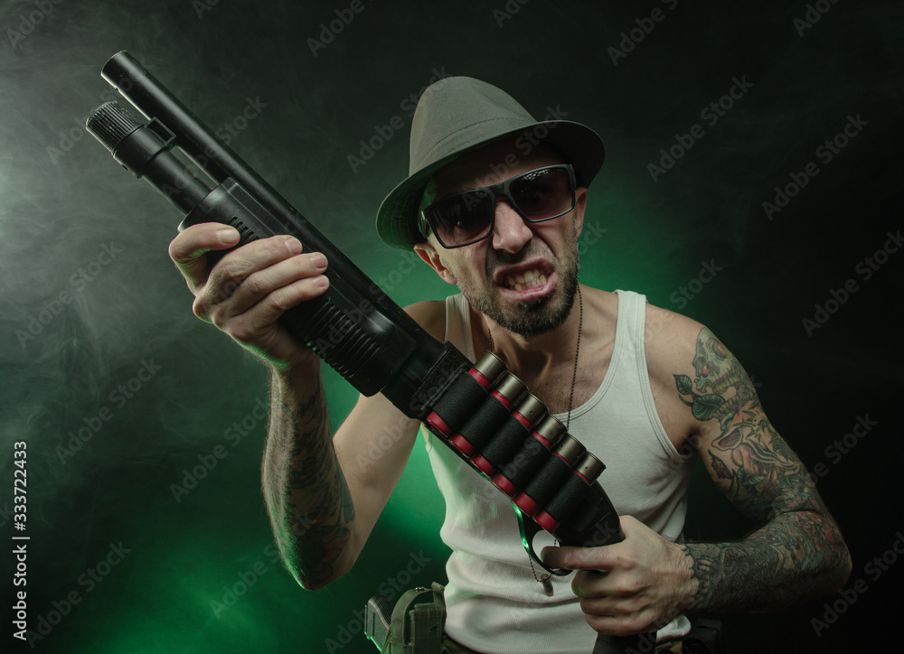 Fototapeta premium an athletic guy with a tattoo poses with a shotgun