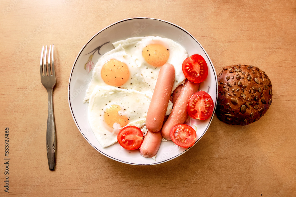 Breakfast of eggs and sausages with a bun on the table Breakfast of eggs and sausages with a bun on the table