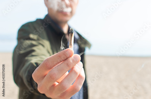 Photography Young man holding a lit marijuana joint while smoking on the beach