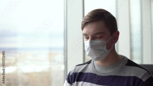 Young man in a medical mask. A man sits in a cafe by the window with a medical mask on his face. Prevention COVID-19.