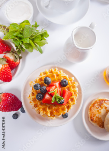 Plate with sweet tasty waffles with honey, berries, cup of tea on the white background.