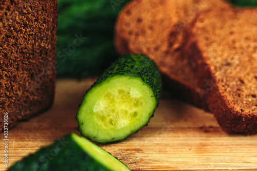 Sliced dark bread on wooden cutting board with sliced cucumbers. Healthy nutrition, healthy food on the table, greens, cucumbers and dark bread.