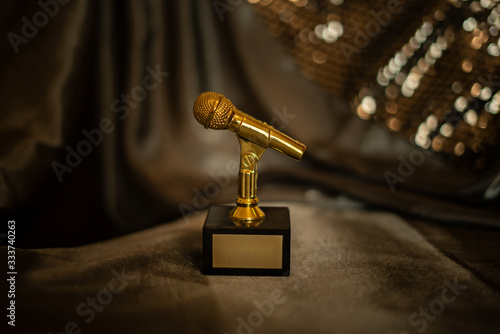 Gold, metallic microphone, mike, mic statuette, figurine medal award for musical achievement with place for title and text of winner on isolated bokeh shiny beaded gold background 