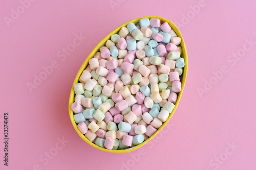 colored mini marshmallows in the shape of an easter egg on a pink background, top view