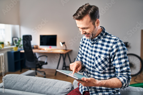Happy adult man using digital tablet while working from home office