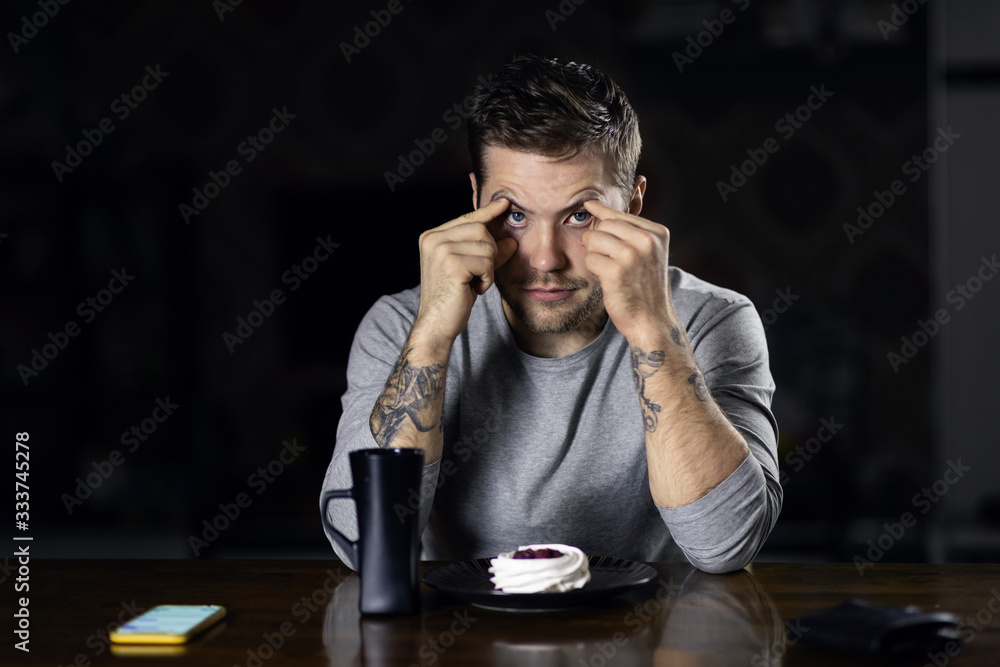 Portrait of a young man of attractive appearance with a beard, mustache and fashionable hairstyle, posing sitting at a table. The concept of combining remote work on the phone and leisure Portrait of a young man of attractive appearance with a beard, mustache and fashionable hairstyle, posing sitting at a table. The concept of combining remote work on the phone and leisure