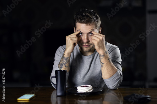 Portrait of a young man of attractive appearance with a beard, mustache and fashionable hairstyle, posing sitting at a table. The concept of combining remote work on the phone and leisure