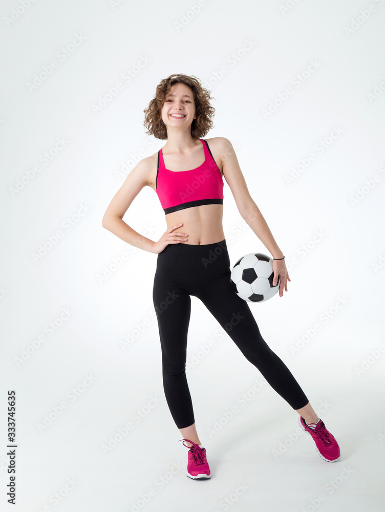 Full length, young athletic woman with a soccer ball in her hands, standing against a gray background and looking at the camera. Full length, young athletic woman with a soccer ball in her hands, standing against a gray background and looking at the camera.