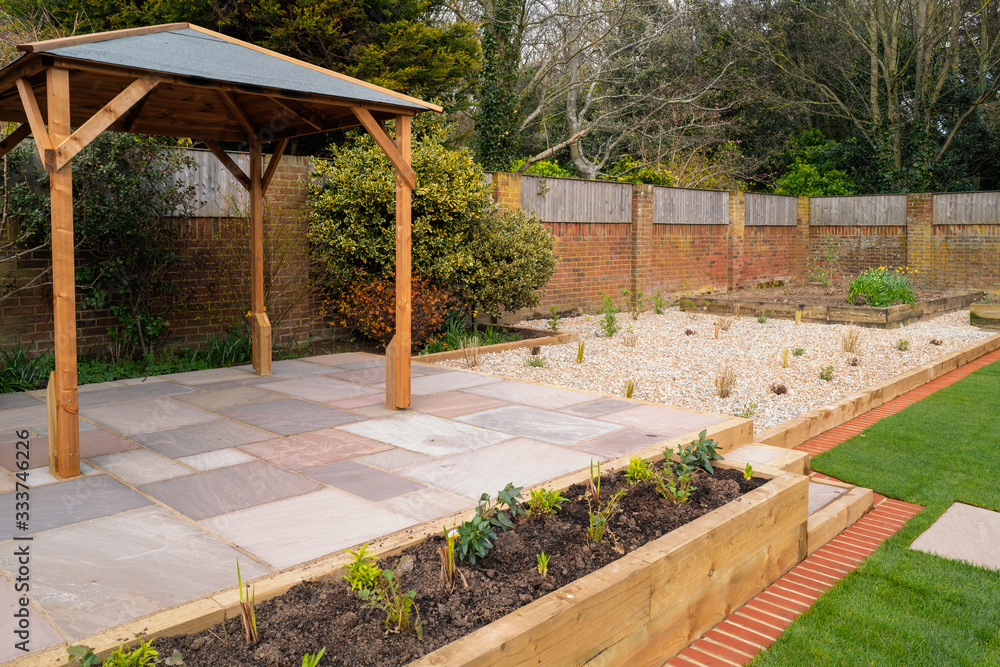 Obraz premium A new raised patio with a wooden gazebo in front of a raised flowerbed and a gravel garden area.