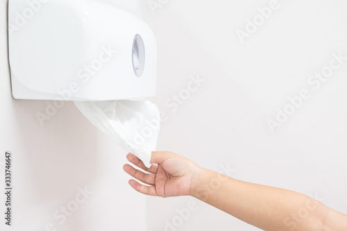Close up woman hand picking white toilet tissue paper for cleaning hand on white wall background.Right hand pull tissue from white plastic box after hand wash in bathroom.