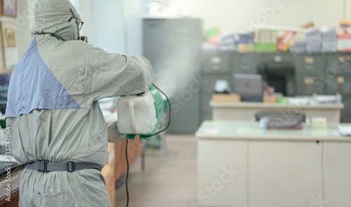 Disinfecting of office to prevent COVID-19, person in white hazmat suit with disinfect in office, coronavirus concept photo