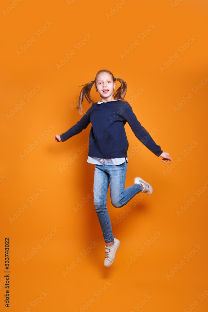 funny little girl in casual clothes jumping on yellow background