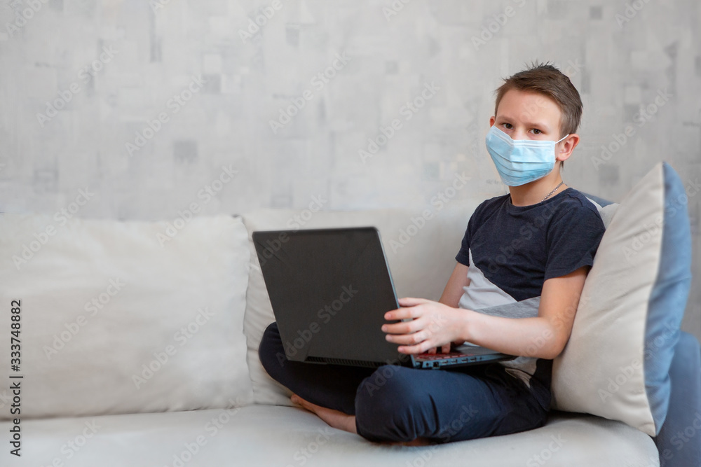 Distance learning in quarantine. A boy in a one-time mask does homework on the couch. Distance learning in quarantine. A boy in a one-time mask does homework on the couch.
