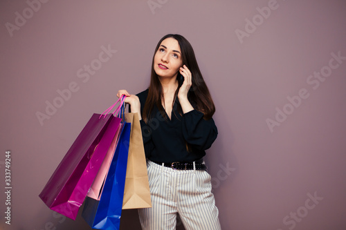 Stunning Happy girl with long brown hair standing with colorful shopping bags and talking on mobile phone, shopping concept, portrait, smiling, looking back.