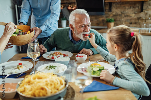 Senior man being feed by his granddaughter at dining table.