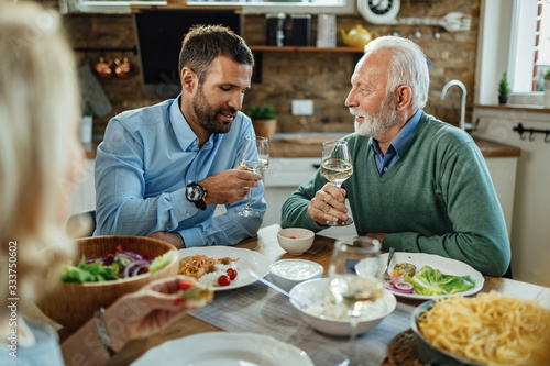 Senior man talking to his adult son while drinking wine during lunch.