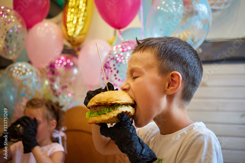 The handsome little boy eating burger in black rubber gloves.