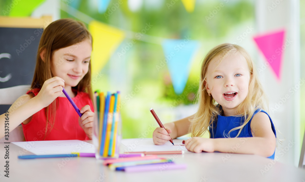 Two sisters drawing with colorful pencils at home. Creative kids doing crafts together. Education and distance learning for kids. Homeschooling during quarantine. Stay at home entertainment. Two sisters drawing with colorful pencils at home. Creative kids doing crafts together. Education and distance learning for kids. Homeschooling during quarantine. Stay at home entertainment.