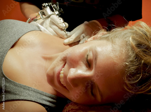 Smiling young woman having tattoo making on shoulder