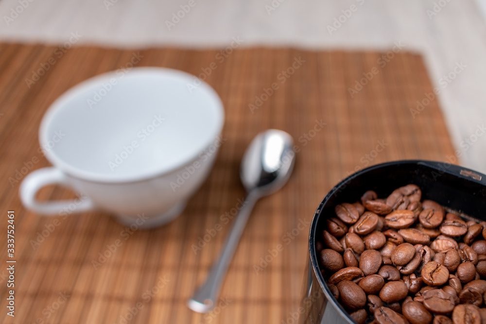 Coffee beans in a electric coffee grinder on a table with a coffee mug. Coffee beans in a electric coffee grinder on a table with a coffee mug.