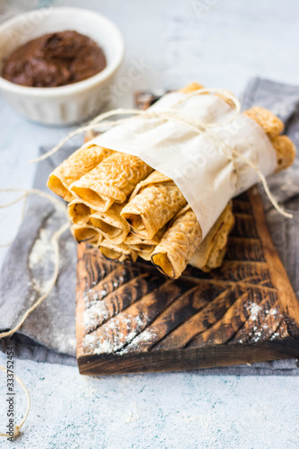 Crepes - sweet thin golden fried pancakes. Vegan, vegetarian dessert. Crepes rolled up into tubes and chocolate sweet hazelnut dessert cream paste