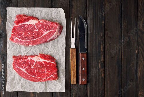 Two fresh slices of beef steak meat on a wooden table with space for text.