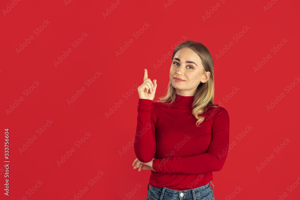 Pointing. Monochrome portrait of young caucasian blonde woman isolated on red studio background. Beautiful female model in shirt. Human emotions, facial expression, sales, ad concept. Youth culture. - obrazy, fototapety, plakaty 