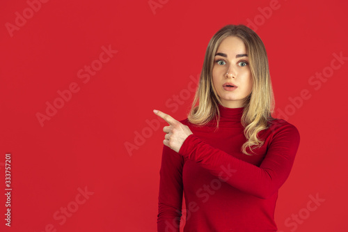 Pointing. Monochrome portrait of young caucasian blonde woman isolated on red studio background. Beautiful female model in shirt. Human emotions, facial expression, sales, ad concept. Youth culture.