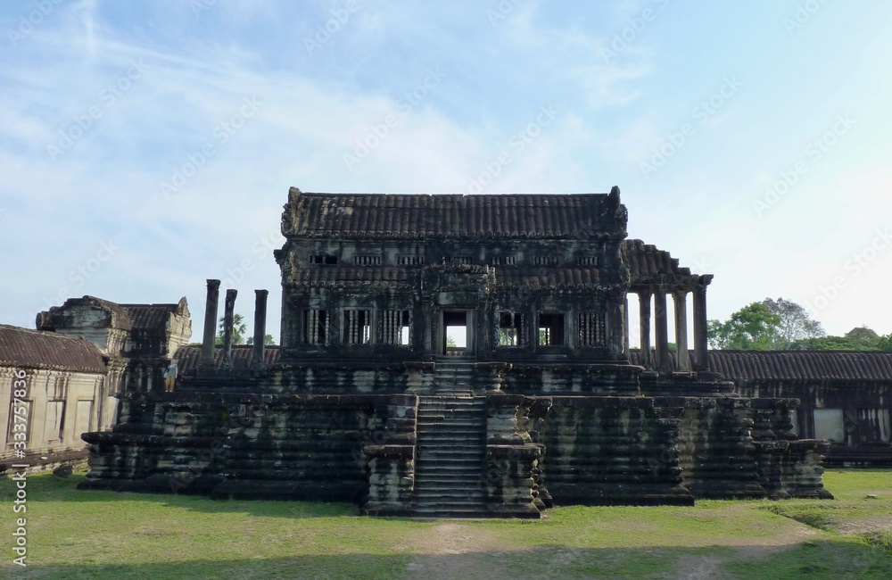 Stone library building of Angkor Wat on green grass before blue sky, ruins of Angkor, Cambodia