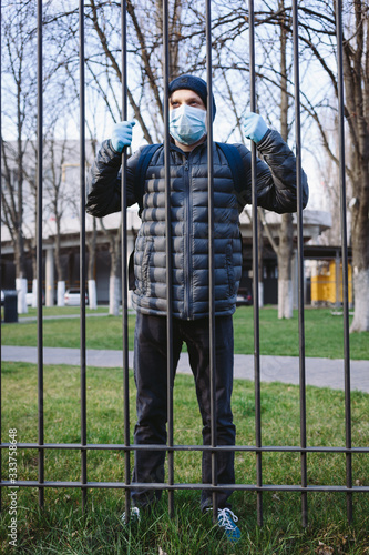 Portrait of young man in surgical mask and gloves near the grid. Pandemic coronavirus 2020. Quarantine. 