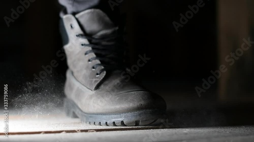 a man walks past the camera, raising dust in the attic into the air. Boot closeup, slow motion