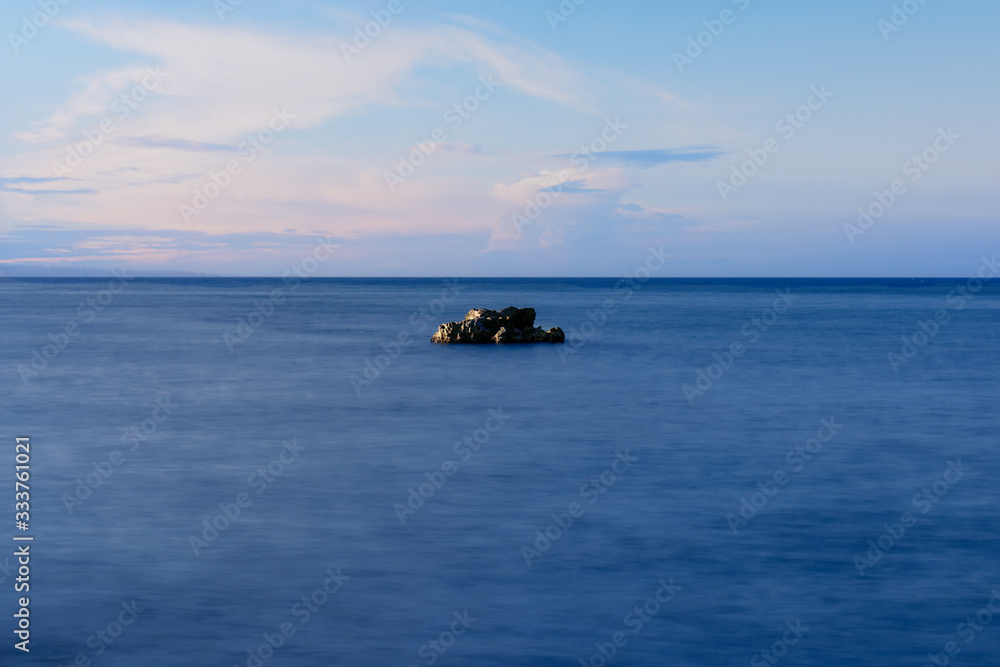 A rock in the middle of the sea. The sky is blue with clouds