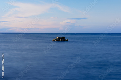 A rock in the middle of the sea. The sky is blue with clouds © Dimitrios