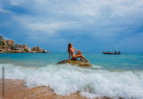 beautiful young woman in bikinis sitting on rock by sea