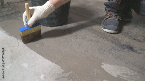 Worker wets the concrete floor with a brush. Primer concrete floor for waterproofing