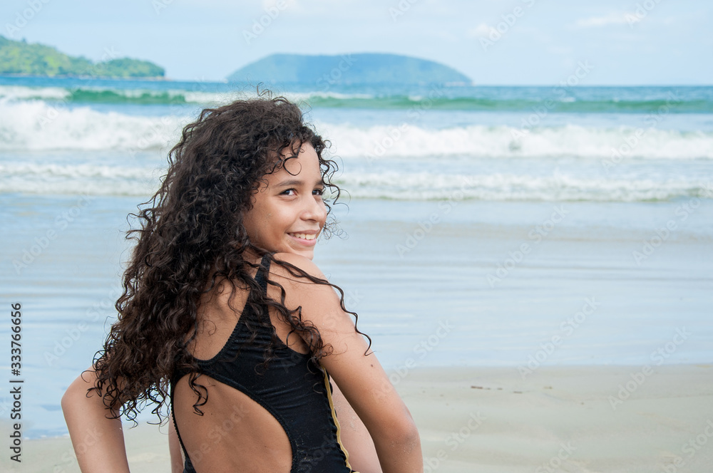 Beautiful latin american girl smiling sitting on a rock at the beach Beautiful latin american girl smiling sitting on a rock at the beach