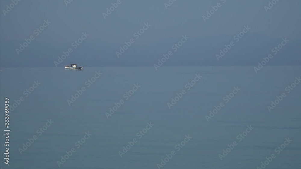 Dolphins enjoy the calm sea. Fishermen are sailing on their small boat.