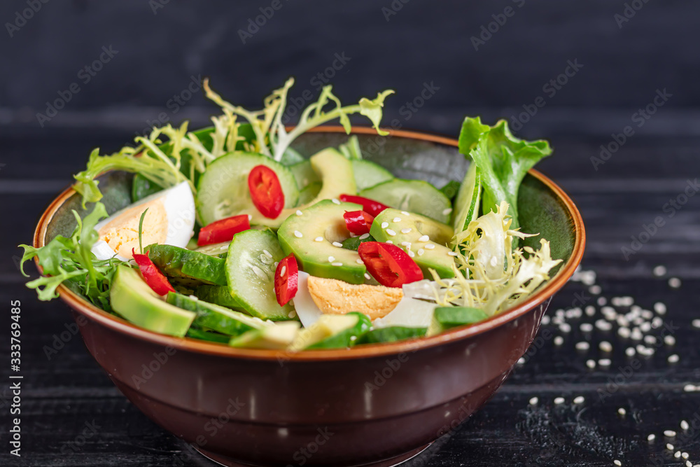 Salad of fresh cucumbers, spinach leaves, arugula, avocado. Served with slices of eggs and red pepper. Dietary nutrition. Breakfast for the whole family. Vitamin plate. On a dark wooden background. Salad of fresh cucumbers, spinach leaves, arugula, avocado. Served with slices of eggs and red pepper. Dietary nutrition. Breakfast for the whole family. Vitamin plate. On a dark wooden background.