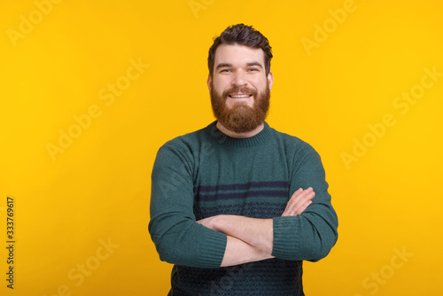 Smiling bearded man with arms crossed is looking at the camera over yellow background.