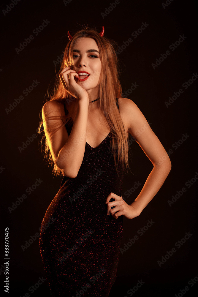 Hot young woman in tight-fitting dress and horns. Costume on halloween, hell, devil. Flashing look. Fashion Style. Hot young woman in tight-fitting dress and horns. Costume on halloween, hell, devil. Flashing look. Fashion Style.