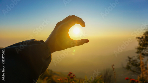 silhouette of hands with beautiful evening sunrise light in hand and blue skyline