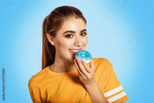 Beauty girl holding blue donuts laughing over white background. There is a dessert, a smile. Beautiful Happy Young woman on party with doughnuts in a yellow shirt. Joyful model Celebrating. photo