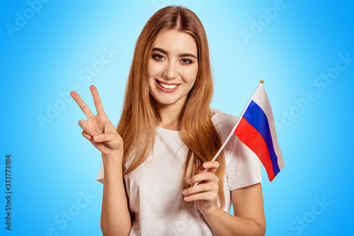 A beautiful young woman holds in her hands the flag of Russia and shows the sign Victoria, Peace, Pacif. Exchange student learning a foreign language. Tourist traveling. photo